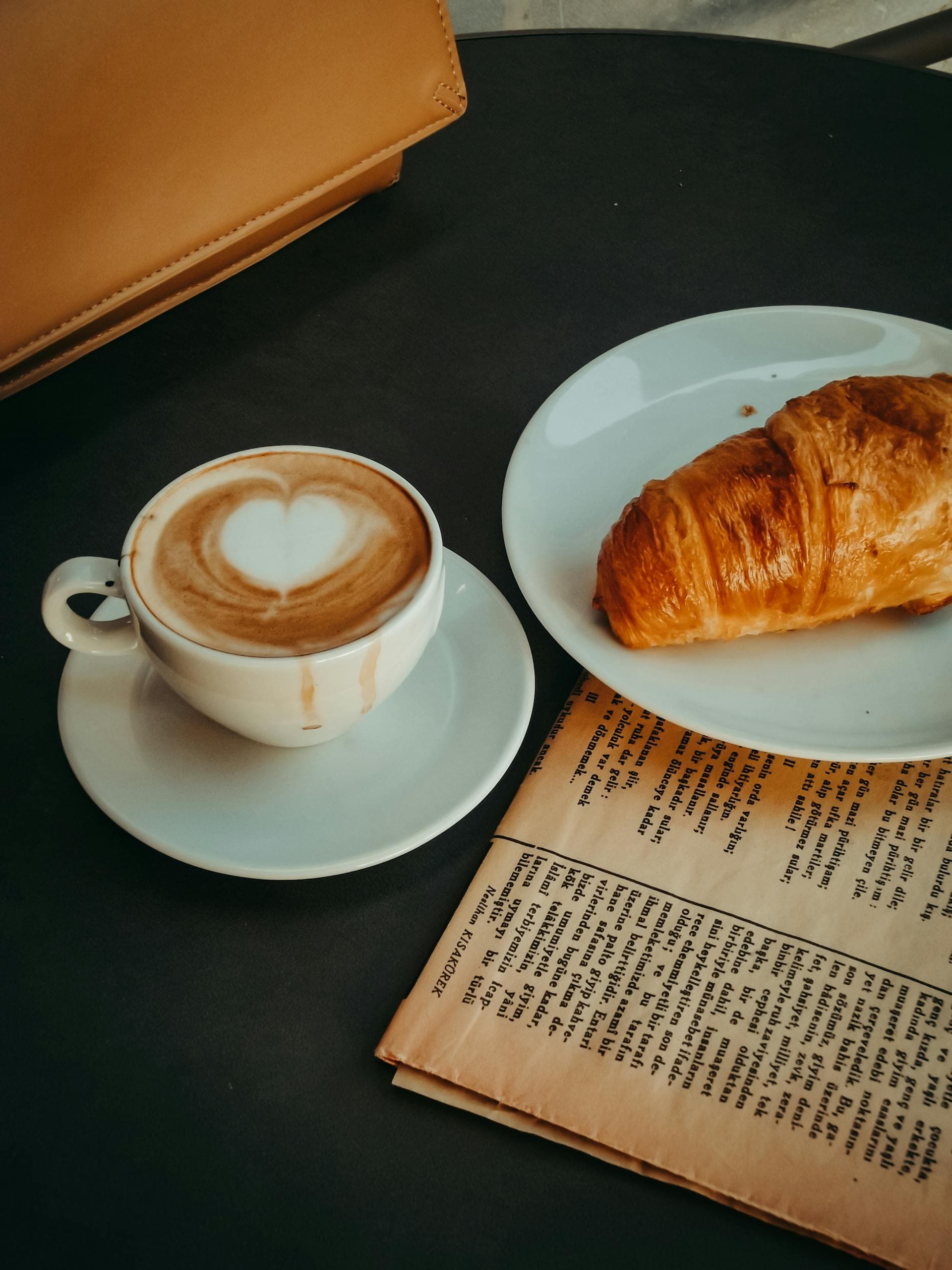 Taza de café con latte art acompañada de un croissant sobre la mesa